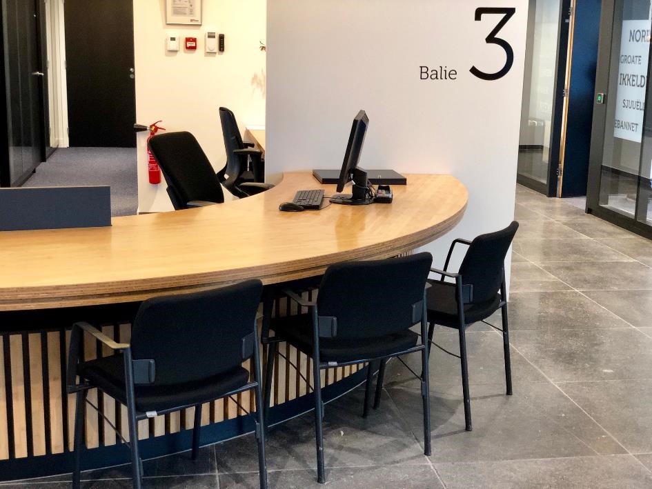 halfronde blankhouten balie met zwarte computer en 3 zwarte stoelen voor bezoekers